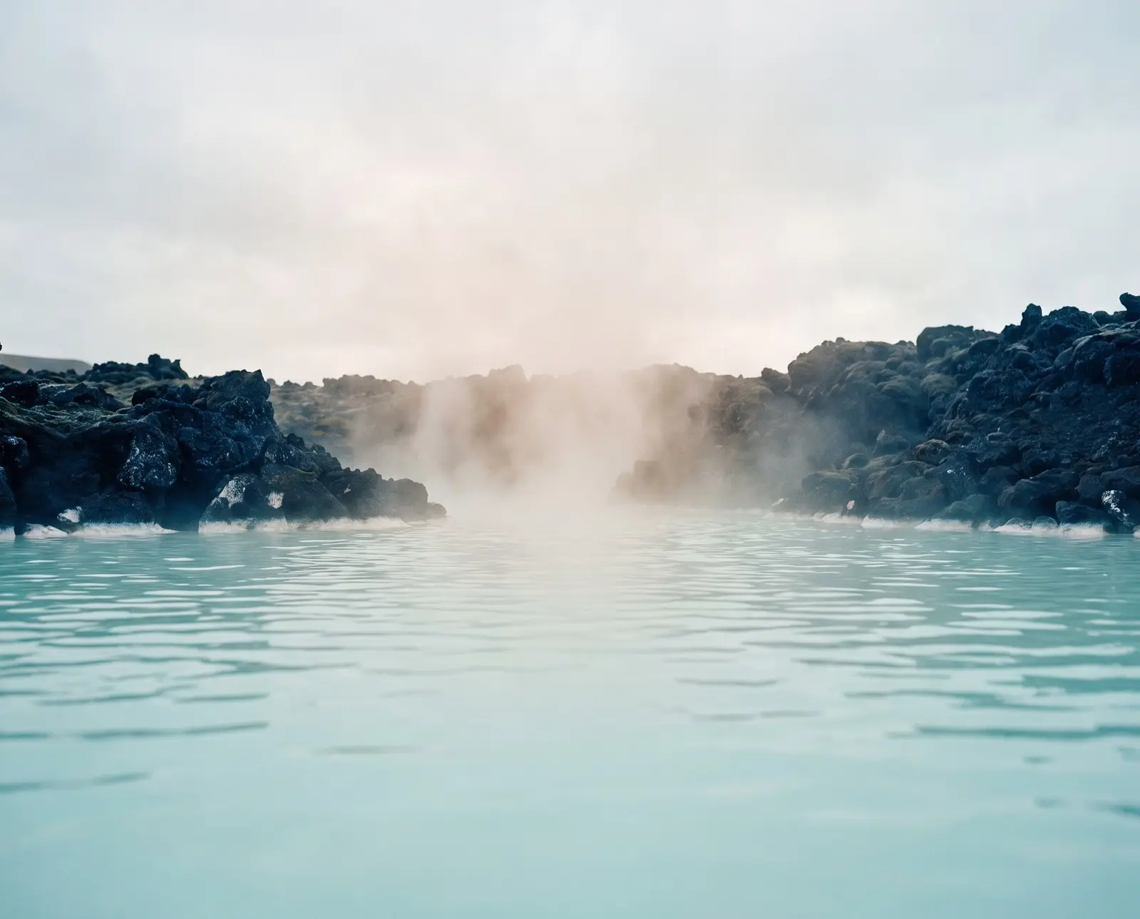 Milky turquoise water and steam among black lava rocks